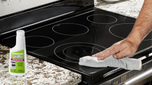 Quelqu'un nettoie une table de cuisson à induction avec un chiffon. Sur le comptoir se trouve une bouteille de nettoyant affresh