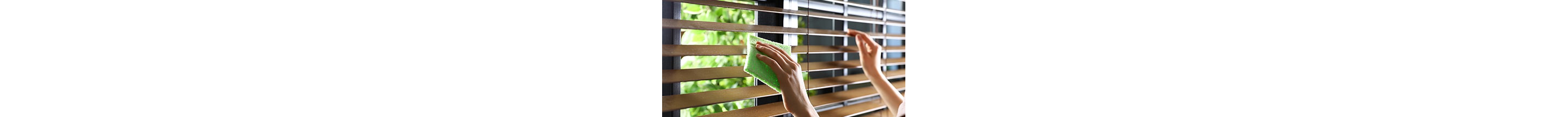 A person dusting wooden window blinds with a cloth.