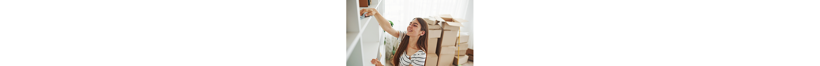 A woman wipes down a shelving unit with moving boxes in the background.